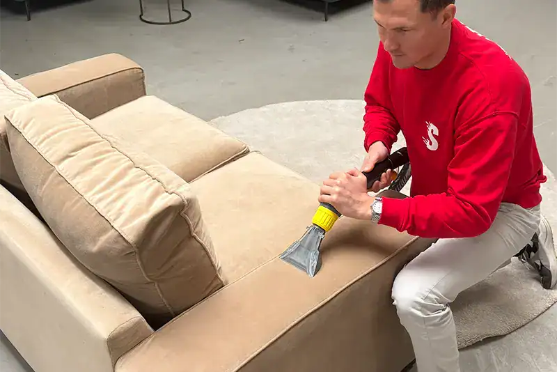 Man reinigt bank met professionele meubelstoomreiniger in woonkamer.